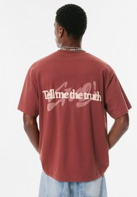 T-shirt en coton bordeaux à manches courtes, avec un texte blanc en gras "Dis-moi la vérité" dans le dos et un design décontracté.