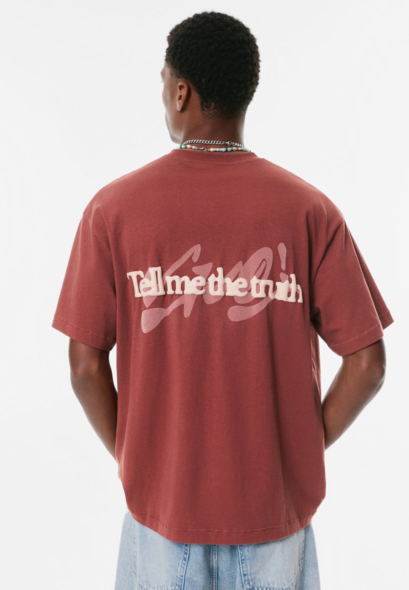 T-shirt en coton bordeaux à manches courtes, avec un texte blanc en gras "Dis-moi la vérité" dans le dos et un design décontracté.