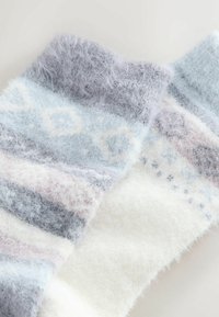 Puhának és bolyhosnak tűnő, szürke, kék és fehér színű, geometrikus mintákkal és texturált csíkokkal díszített kötött zoknik.