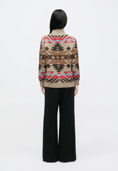 Strikket sweater i beige med geometriske mønstre i brunt, rødt og blåt. Har høj krave og ribbet kant. Kombineret med brede sorte bukser.