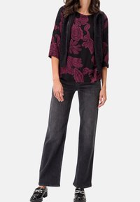 Top negro con patrón floral burdeos, combinado con jeans de pierna ancha oscuros. La modelo lleva un chaleco de piel sintética negro y unos mocasines negros brillantes.