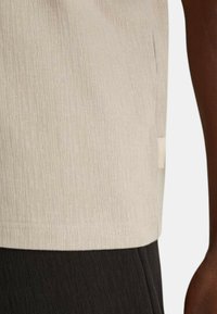 Camicia corta beige chiaro testurizzata con orlo dritto e spacco laterale, abbinata a tessuto nero a coste scuro.