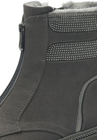 Bottine en suède gris avec fermeture éclair sur le côté, panneaux texturés ornés de petits clous et doublure douce, conçue pour le confort et le style.