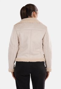Giacca beige foderata in shearling con design accorciato e colletto ampio. Texture morbida e dettagli delle cuciture, con chiusura e orlo regolabile.