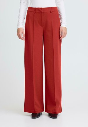 Wide-legged, high-waisted trousers in rust red, made from smooth fabric with front pleats. Minimalist design, no visible hardware or patterns.