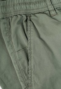 Close-up of green fabric pants with visible elastic waistband and side pocket stitching details.