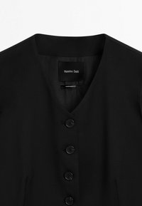 Gilet nero senza maniche con scollatura a V e quattro bottoni neri, etichettato Massimo Dutti, prodotto in Marocco.