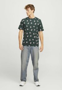 Mørkegrønt t-shirt med blomsterprint i hele, rund halsudskæring, korte ærmer, parret med løstsiddende lys blå jeans.