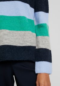 Maglione a righe con colori blu navy, verde, grigio e azzurro chiaro; realizzato in morbido tessuto a maglia strutturato; presenta un ampio polsino a coste.