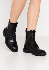 Botas de tobillo de cuero negro con textura de cocodrilo, frente con cordones, cremallera lateral y suela de goma gruesa.