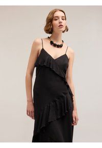 Rochie neagră din satin, cu detalii volănuțe, bretele subțiri și un design fluid. Purtați cu un colier masiv negru și auriu.