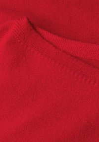 Roter Kaschmirstoff mit weicher Textur, sichtbarem feinen Strick und gerippten Kanten. Die Farbe ist einheitlich, ohne auffällige Muster oder Verzierungen.