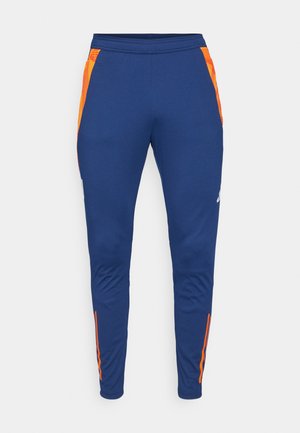 Marineblauwe sportbroek met oranje zijdetails, tapered fit, elastische tailleband en een gladde textuur. Inclusief subtiele merkvermelding op het been.