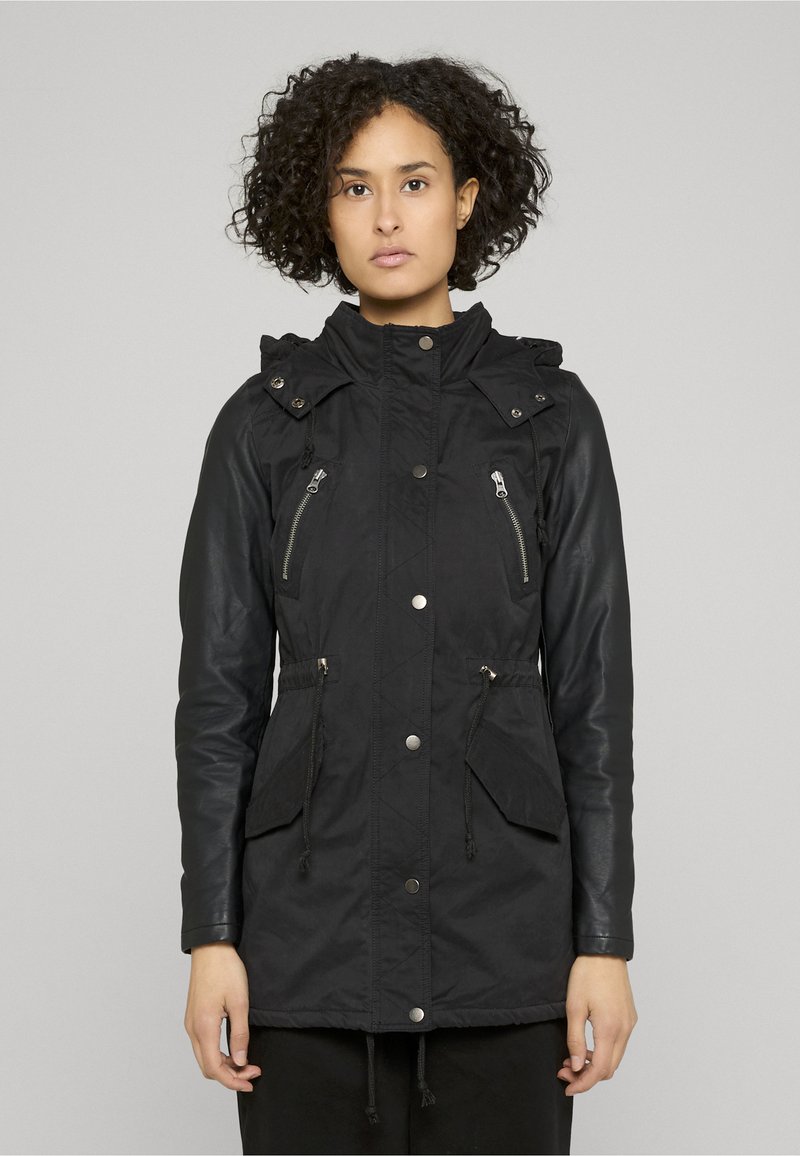 Fekete dzseki vegyes anyagból készült kialakítással, párnázott testtel és bőr ujjakkal. Cipzáras zsebekkel és húzózsinóros derékkal rendelkezik.