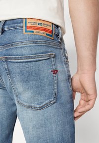 Ljusblå denimjeans med en synlig brun l äderetikett vid midjan, med röd sömnad och två bakfickor.