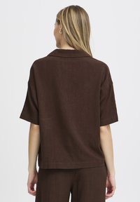 Chemise en lin marron à manches courtes avec col. Coupe décontractée, design simple et surface texturée, présentée de dos.