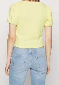 Keltainen ribbikankainen lyhyt toppi puffi hihalla, yhdistettynä vaaleansinisiiin farkkuihin, joissa on takataskut ja istuva vyötärö.