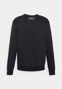 Musta pitkähihaisella Nike huppari näkyy takaa, jossa on pieni harmaa Nike logo lähellä kaula-aukkoa.