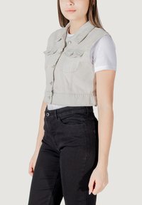 Gilet in denim grigio chiaro, cropped, con colletto a punta, tasche frontali e bottoni argentati, abbinato a jeans neri aderenti.