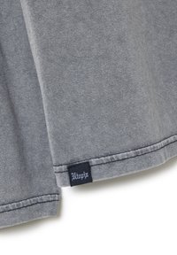 Graues Baumwoll-T-Shirt mit rundem Halsausschnitt, kurzen Ärmeln und einem genähten Saum, mit einem schwarzen Markenetikett auf der unteren linken Seite.