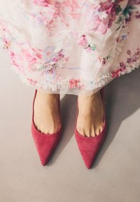 Piros velúr hegyes orrú magassarkú, sima textúrával, virágmintás hímzett áttetsző ruhával párosítva, fodros részletekkel az alján.