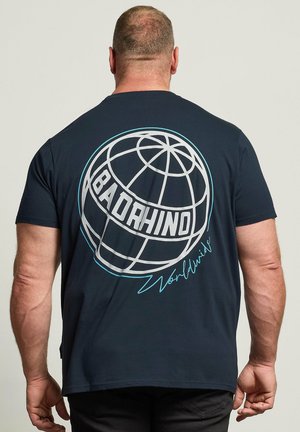 Uomo che indossa una maglietta blu navy mostrando la schiena con un design a globo e testo "BADRHINO Worldwide" in bianco e azzurro chiaro.