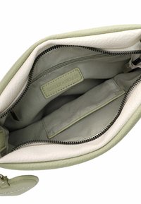 Grøn og creme læder taske indvendigt med en lynlåslomme, glat tekstur og mærkeetiket, indeholdende en rummelig hovedlomme og en sidelomme.