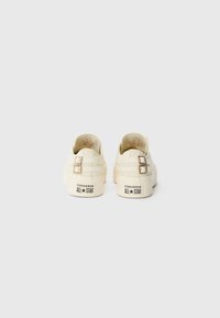 Kremaste Converse All Star tenisice s dva remena na kopčanje, teksturirani platneni gornji dio, zaobljeni vrh i gumeni potplat s detaljima logotipa.