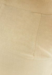 Ljusbeige tygprov med en slät textur och subtil lyster. Inkluderar en synlig söm med en lätt fickdetalj.