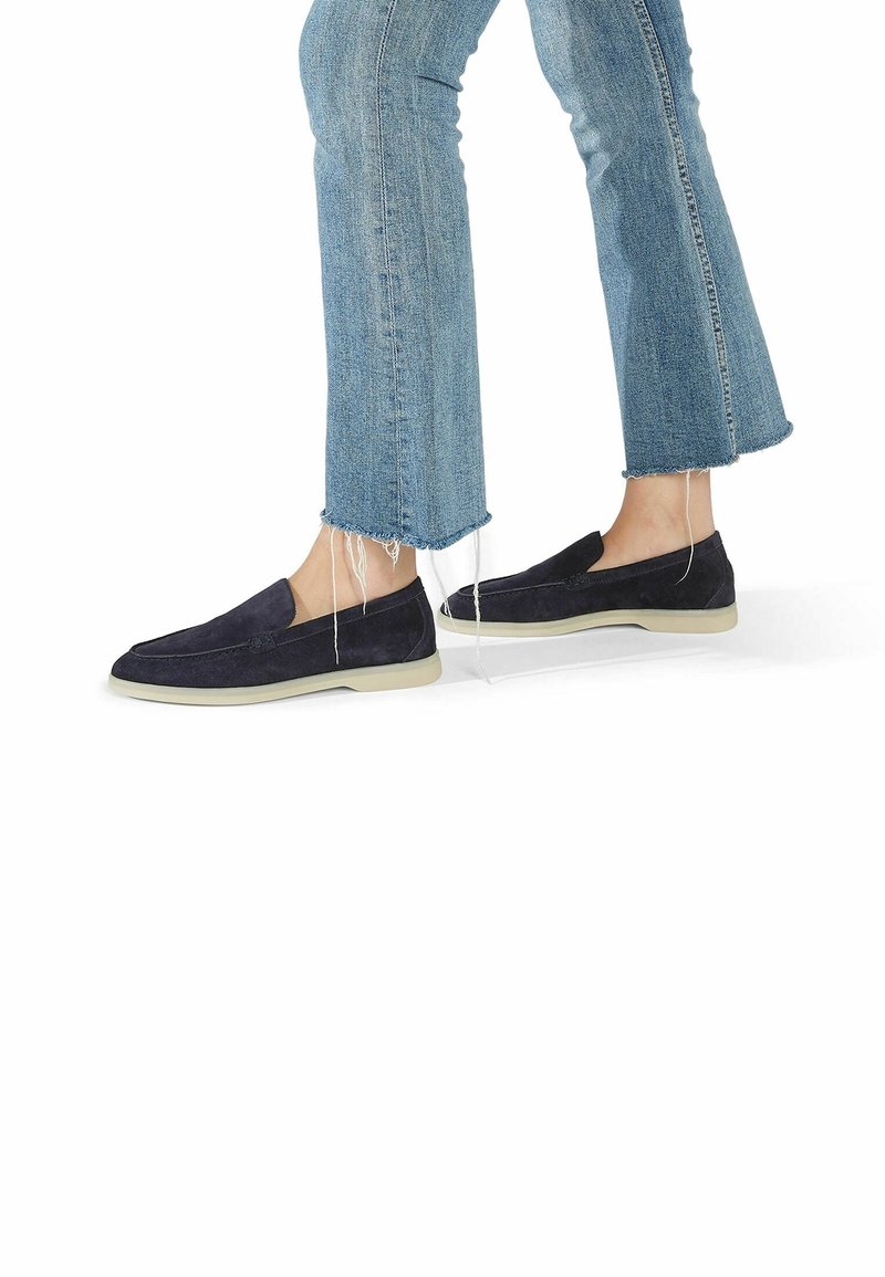 Chaussures en daim bleu marine à enfiler avec une semelle blanche profilée basse, associées à un jean bleu clair à ourlet effiloché. Caractérisées par une finition lisse et des détails minimalistes.