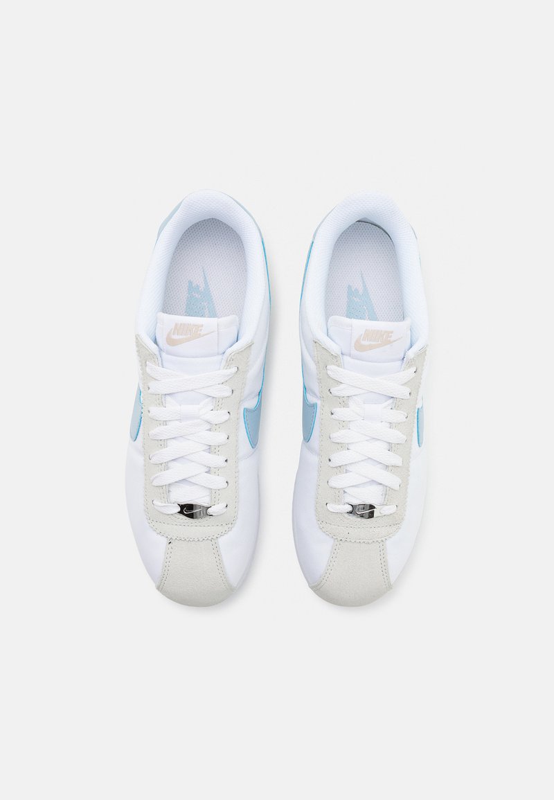 Baskets blanches avec des accents bleu clair, des superpositions en daim et un design de laçage à l'avant. Comprend une languette en maille et un œillet en plastique argenté.