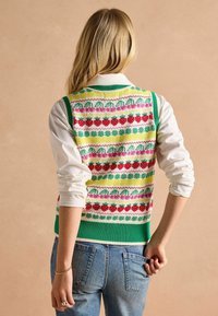 Strickweste mit mehrfarbigen Mustern aus Erdbeeren und Blumen auf einem hellgelben Hintergrund, die mit einem grünen Rippenbund abgeschlossen ist.