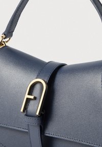 Tengerészkék bőrtáska strukturált formával, aranyszínű fém kiegészítővel és varrási részletekkel a fedél és a pánt mentén.