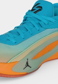 Φωτεινό μπλε αθλητικό παπούτσι με πορτοκαλί λεπτομέρειες στη σόλα, μαύρο λογότυπο Jumpman, πάνελ από δίχτυ και λεπτομερές κορδόνι σε εξωτερικό μέρος με κλιμακωτό πλέγμα.
