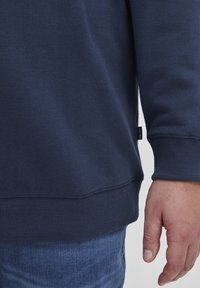 Felpa blu navy con polsini e orlo a costine, realizzata in tessuto liscio, con un piccolo etichetta del marchio sul lato vicino al fondo.
