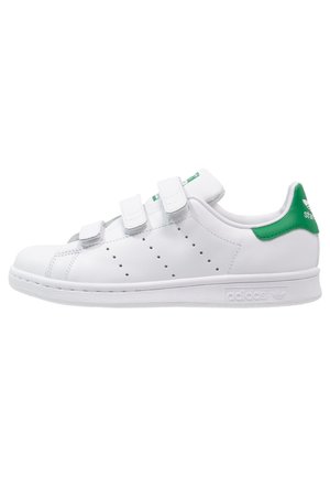 Zapatilla blanca de Adidas con tres tiras de velcro, franjas laterales perforadas y una lengüeta verde en el talón con el logo de Adidas.