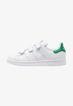 Baskets blanches Adidas avec trois bandes auto-agrippantes, des bandes latérales perforées et un onglet de talon vert avec le logo Adidas.