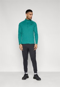 Αθλητικό τοπ μακρυμάνικο σε τιρκουάζ με ημιδιάφανο φερμουάρ και μαύρο λογότυπο, συνδυασμένο με μαύρο στενό παντελόνι και μαύρα αθλητικά παπούτσια. Απλός σχεδιασμός, άνετη εφαρμογή.