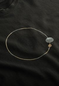 Zwarte katoenen t-shirt met een ronde grafische ontwerp in het wit, grijs en lichtbruin, dat hemelse vormen in een minimalistische stijl afbeeldt.
