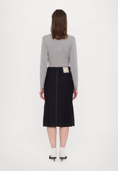 Szürke hosszú ujjú felső, fekete farmer szoknya oldalsó hasítékokkal, látható narancssárga cérnával, és egy 'MM' felirattal ellátott címke a deréknál.