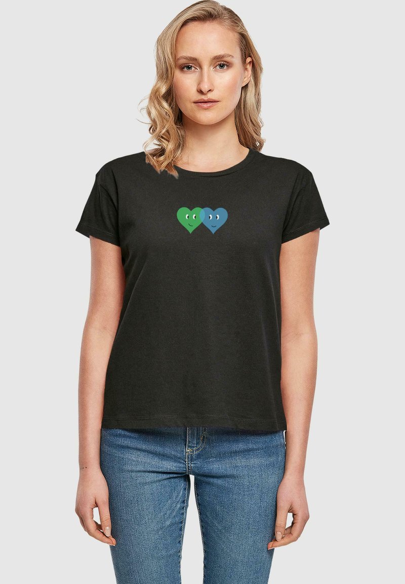 Schwarzes T-Shirt mit kurzen Ärmeln, das ein grafisches Motiv von zwei Herzen zeigt, eines grün und eines blau, mit Gesichtern, zentriert auf der Brust. Lässige Passform.