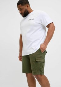 Camiseta blanca de manga corta con texto negro en el pecho, combinada con pantalones cortos cargo verde oliva que tienen bolsillos laterales y un ajuste relajado.
