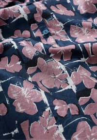 Ingrandimento di un tessuto blu navy con stampa floreale di ibisco rosa e un bottone blu scuro, che mostra texture e pieghe.