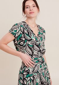 Robe fleurie avec une base noire, des motifs de feuilles blanches et vertes, des manches courtes et un décolleté en V. Tissu doux avec une coupe fluide.