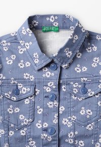 Giacca di jeans blu con stampa floreale bianca, chiusura con bottoni, due tasche a patta sul petto e colletto.