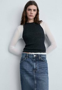 Zwart geribbeld tanktop over een witte lange mouw shirt, gecombineerd met een hooggetailleerde denim rok in een middelmatige wassing.