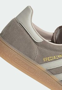 Γκρι σουέντ αθλητικό παπούτσι με ανοιχτό γκρι δερμάτινες λεπτομέρειες, στρογγυλεμένη φτέρνα, με χρυσή επιγραφή "SPEZIAL" και λαστιχένια σόλα με σχέδιο.
