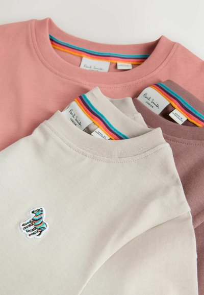 Drei übereinandergelegte T-Shirts in Rosa, Beige und Dunkelrosa. Jedes hat einen regenbogenfarben gestreiften Halsausschnitt und eine blaue Zebra-Stickerei auf dem beigen Shirt.