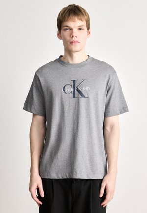 T-shirt en coton gris avec des manches courtes et un col rond, orné d'un logo graphique bleu marine "Calvin Klein" et "CK" sur le devant.