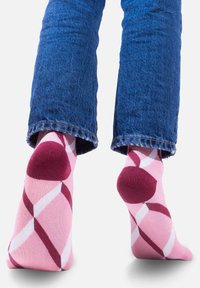 Różowe skarpetki z geometrycznym wzorem w diamenciki w kolorze białym i burgundowym. Wzmocnione pięty i palce, noszone z krótkimi niebieskimi dżinsami.